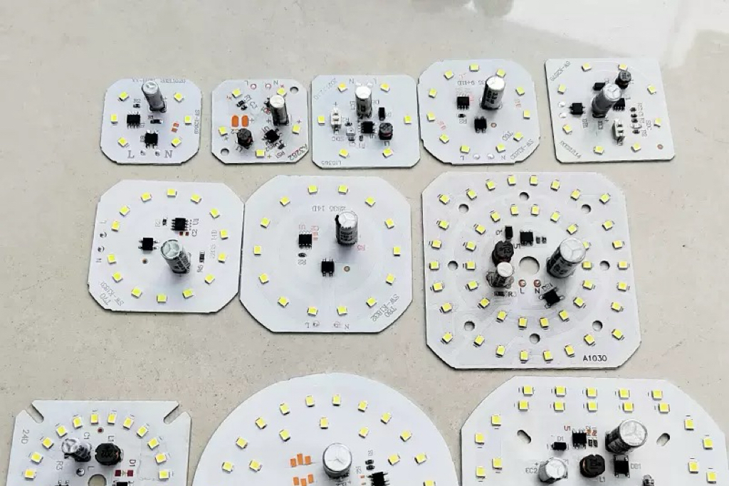 Circular printed circuit board designed for driver-on-board LED light bulb, populated with multiple small square surface mount LED chips around the perimeter and tiny black rectangular resistors in the center, bare aluminum substrate, technical close-up view